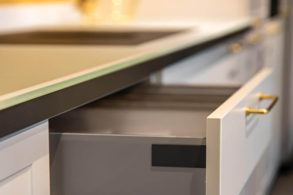 Close-up of a kitchen countertop edge above an open cabinet drawer with a brass handle