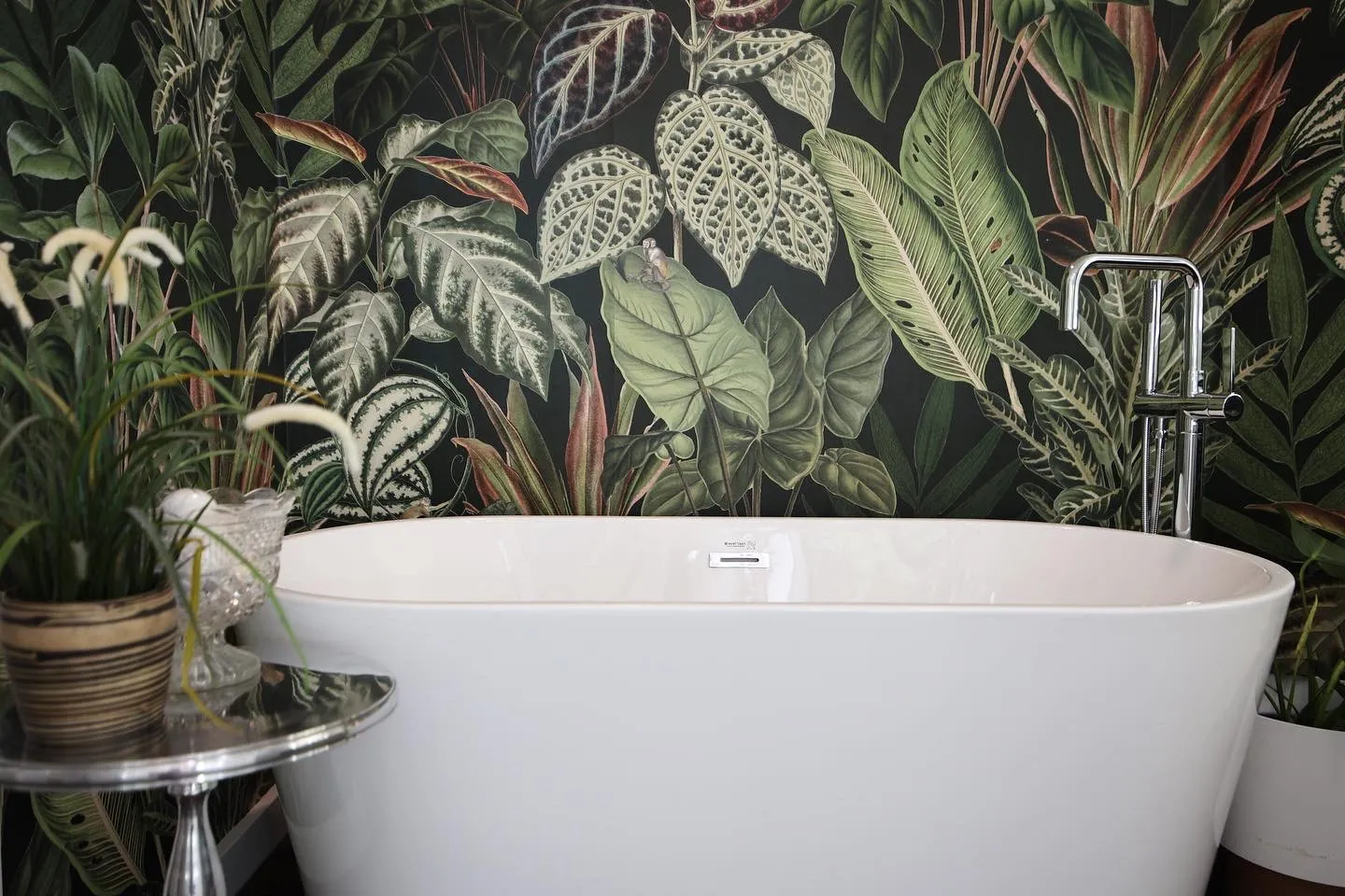 Freestanding tub against a botanical mural wall with a floor-mounted filler, in a tropical-themed bathroom remodel